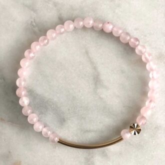Rose quartz beaded stretch bracelet with a 14k gold-filled curved bar and starburst bead on a light marble background.