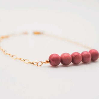 Rhodonite Genesis bracelet with pink gemstone beads and a gold-filled chain on a white background.