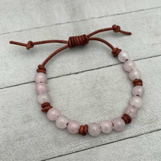Adjustable rose quartz bead bracelet on brown leather with sliding knot clasp on a gray wooden background.