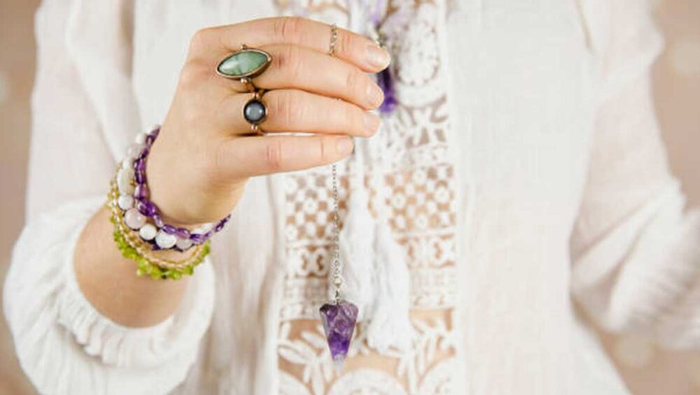 Woman holding amethyst pendulum with gemstone bracelets, symbolizing types of healing jewelry for mind, body, and spirit