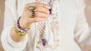 Woman holding amethyst pendulum with gemstone bracelets, symbolizing types of healing jewelry for mind, body, and spirit
