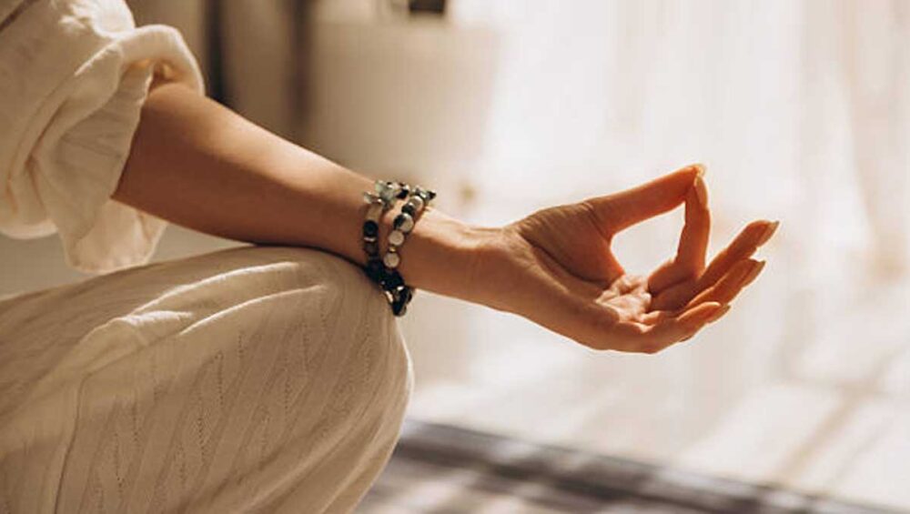Woman meditating wearing gemstone meditation jewelry bracelet on wrist