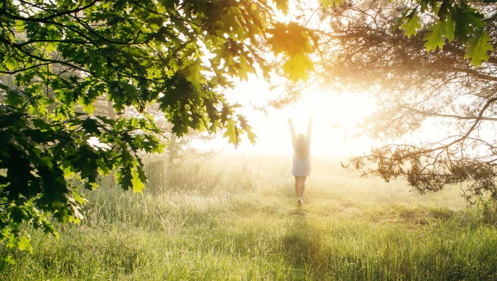 woman standing in sunlight through trees practicing morning grounding ritual