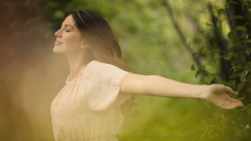 woman standing in nature with open arms, embracing light and practicing energetic self-care