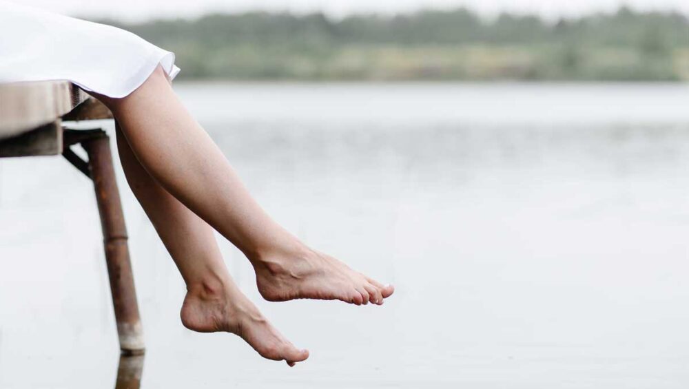 bare feet over calm lake symbolizing grounding with water and emotional healing