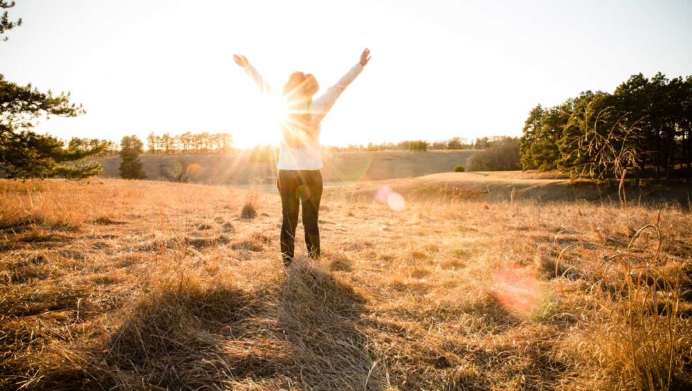 person standing in a sunlit field with arms raised, symbolizing healing and emotional freedom