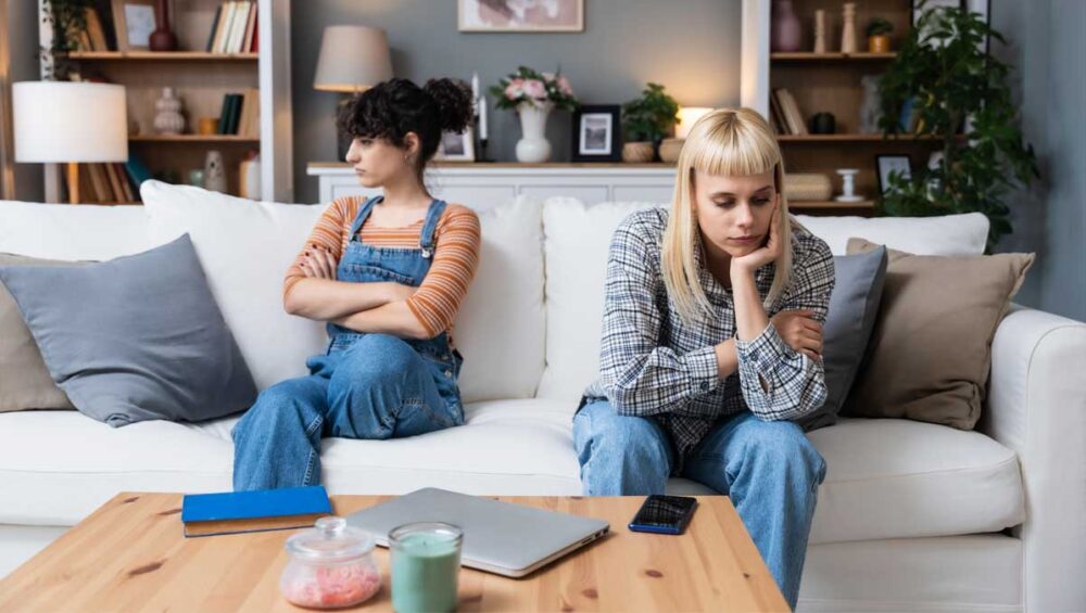 two distant siblings sitting apart on a couch looking upset