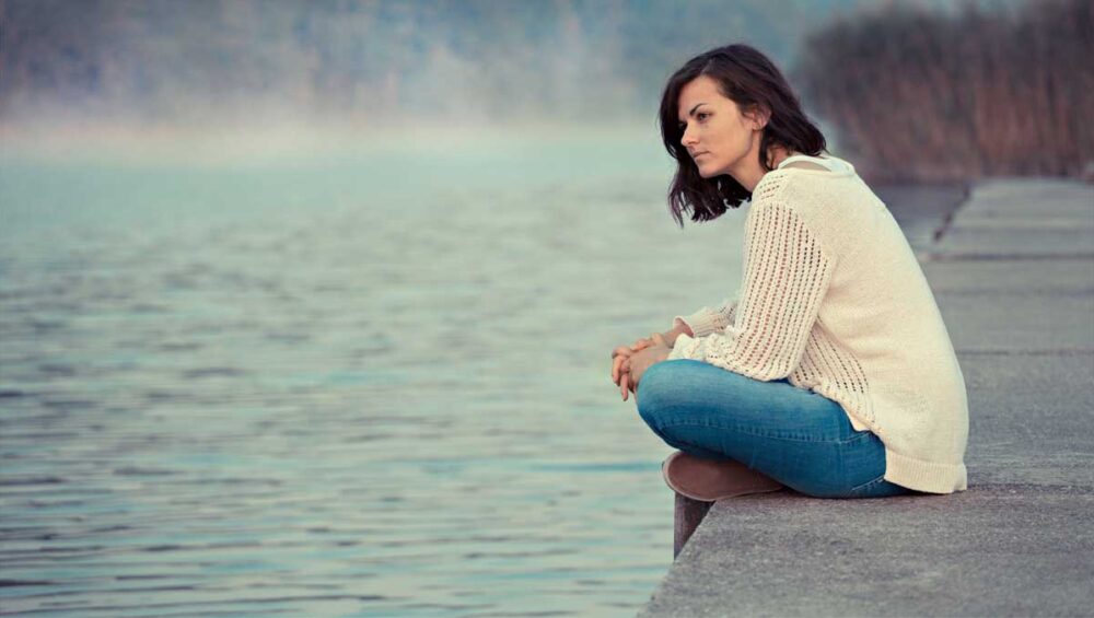 Person sitting by a calm lake reflecting on life, symbolizing self-awareness and emotional healing.