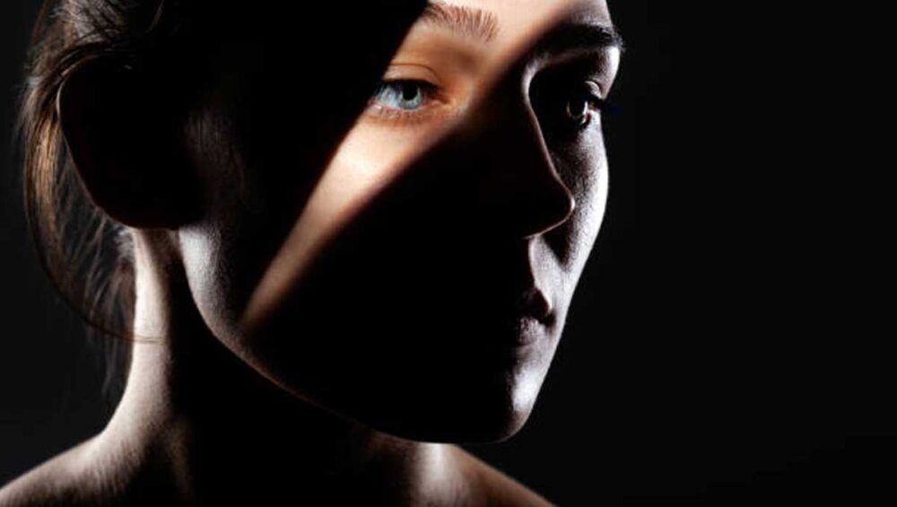 woman’s face partially lit in dramatic shadows symbolizing dual empathy and darkness