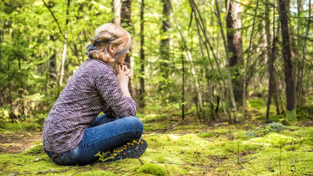 woman sitting peacefully in a sunlit forest, grounding and reflecting