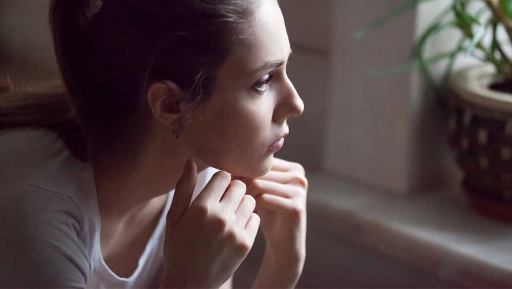 woman looking out the window with a thoughtful expression, representing the impact of rejection trauma