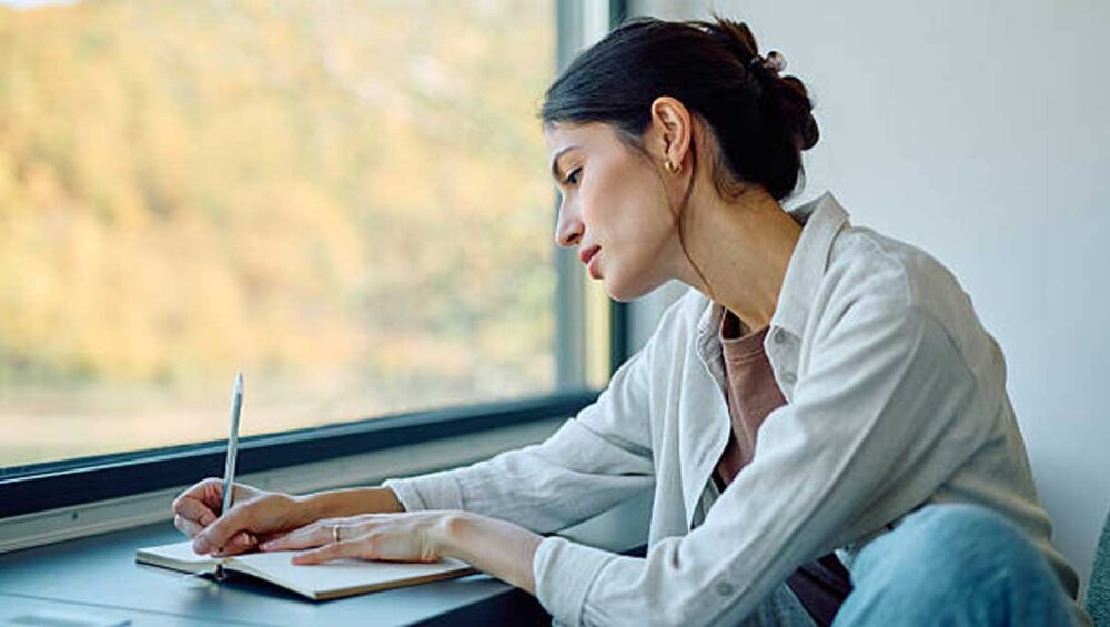 woman journaling by a window to support emotional stability and self-regulation