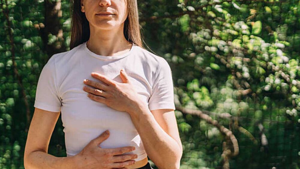 person practicing nervous system regulation techniques with one hand on chest and one on belly in nature