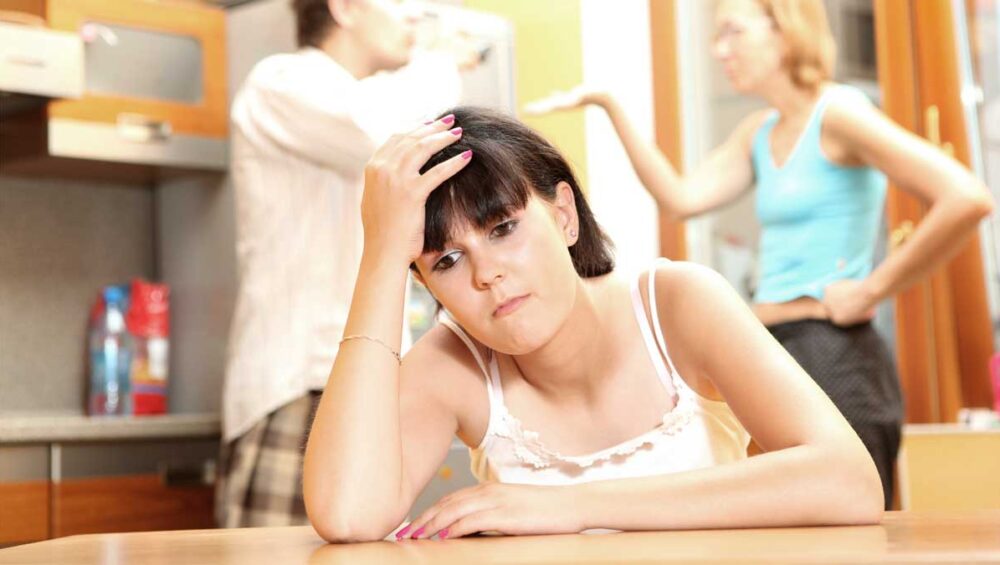 young woman feeling blamed while parents argue in the background, representing the family scapegoat role