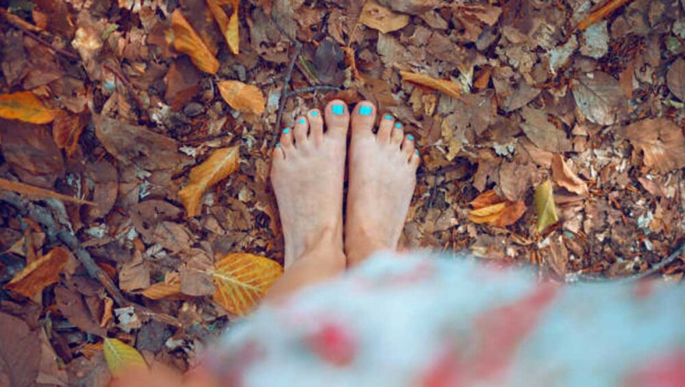 Bare feet standing on fallen autumn leaves outdoors