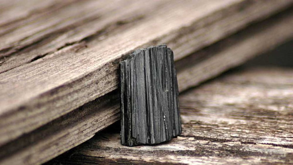 A raw black tourmaline crystal resting against weathered wood.