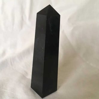 Polished black tourmaline tower with a faceted point, standing upright against a light fabric background
