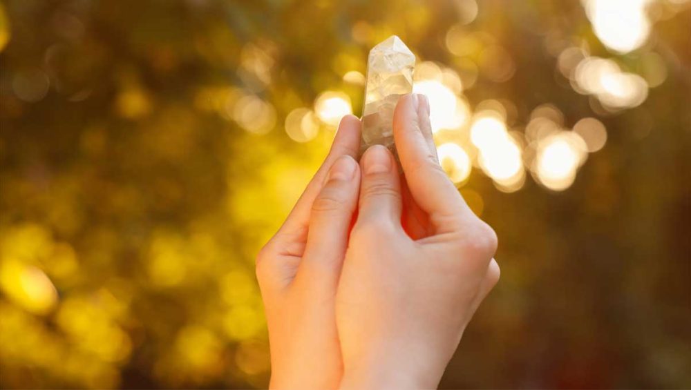 Hands holding a citrine crystal in warm sunlight with a soft golden background