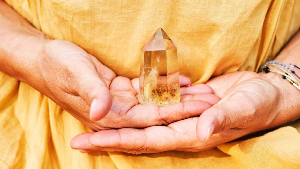 Hands holding a citrine crystal point against a warm yellow background