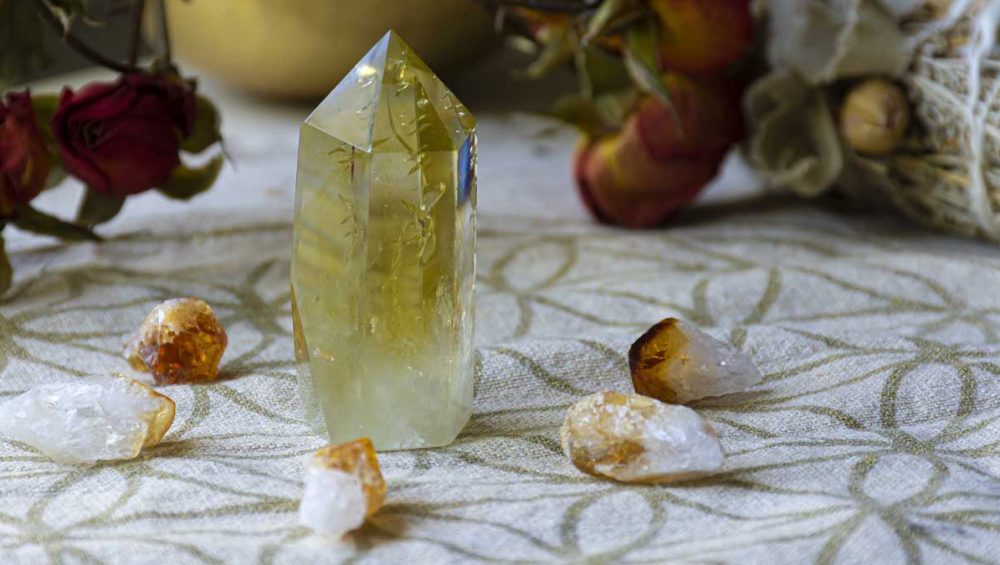 Yellow citrine crystal point standing on patterned fabric with small raw citrine stones around it