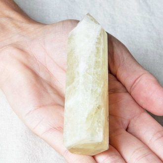 Polished citrine tower held in a hand, showing pale yellow color, natural inclusions, and a faceted point
