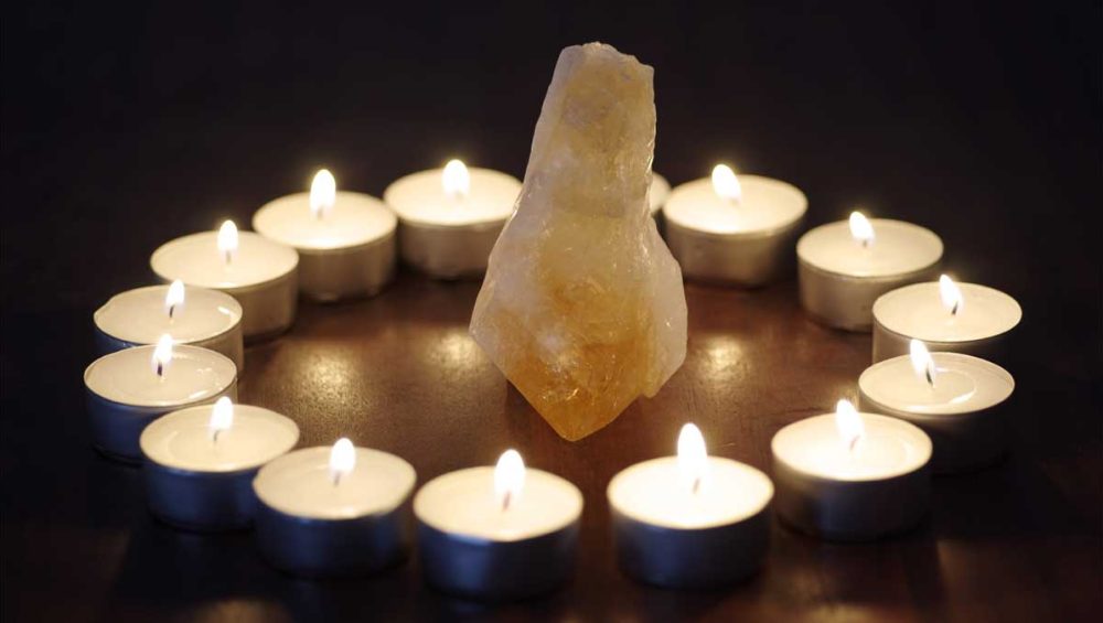 citrine crystal surrounded by lit tea candles in a dark setting