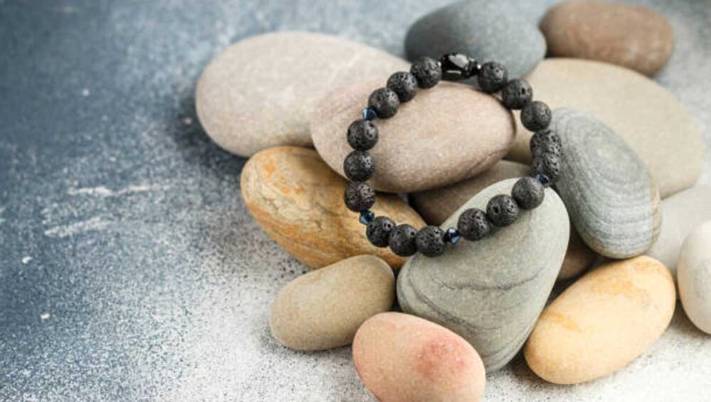 Black beaded grounding bracelet resting on smooth neutral-toned stones on a textured gray surface