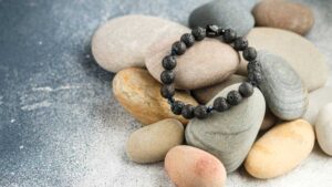 Black beaded grounding bracelet resting on smooth neutral-toned stones on a textured gray surface