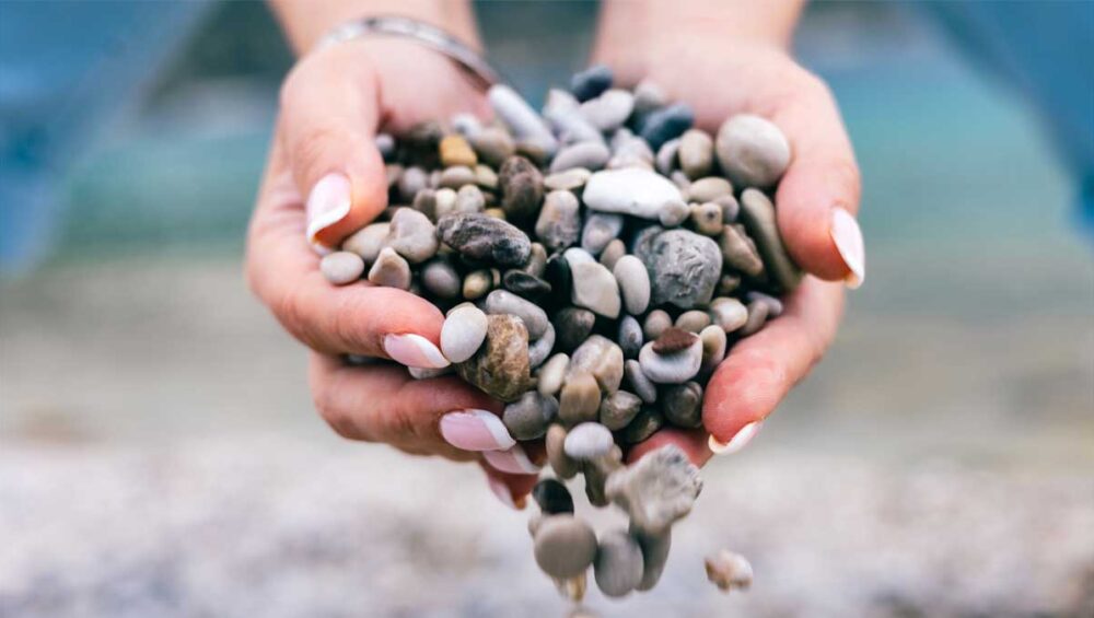 Hands gently holding small stones as they fall naturally