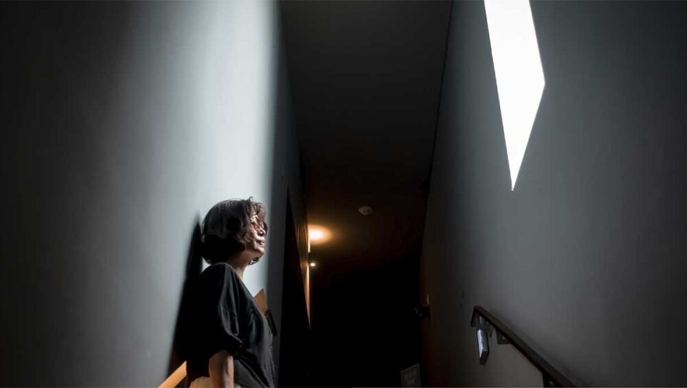 Person standing in a narrow, dimly lit corridor looking toward a bright opening above