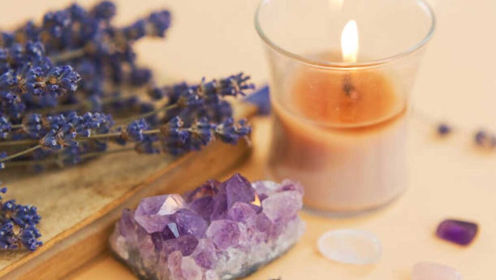 Lavender sprigs beside a lit candle and purple crystal cluster on a light background