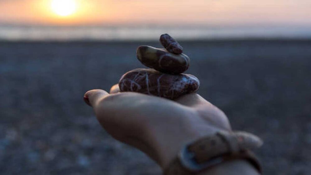 Hand holding stacked smooth stones on a beach at sunset