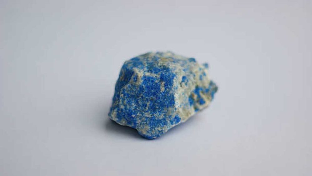 Raw lapis lazuli stone on a clean white background, highlighting its natural blue color and texture.