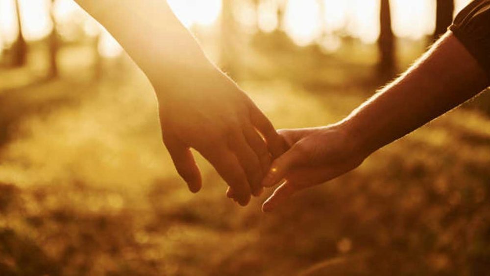 Two people holding hands outdoors in warm golden sunlight
