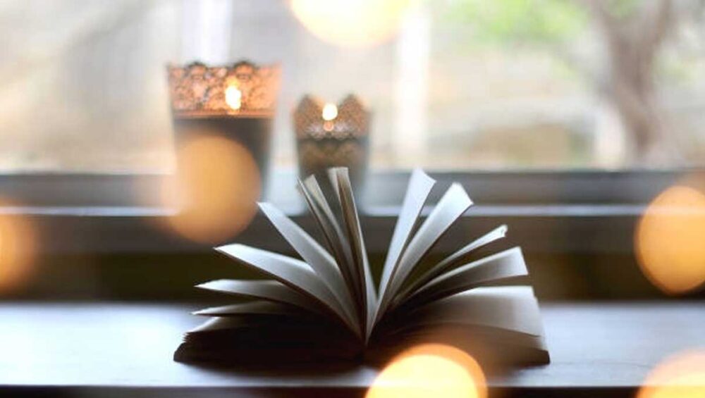 Open book on a windowsill with soft candlelight and warm blurred lights in the background