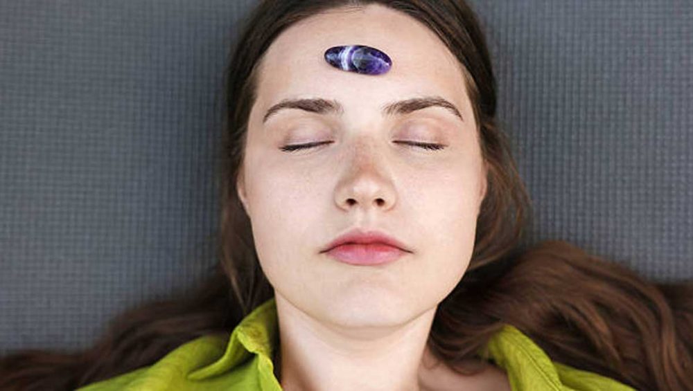 A woman resting with a polished amethyst stone placed on her forehead