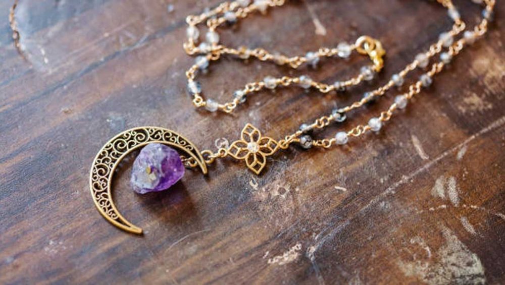 Amethyst crystal pendant necklace with a crescent moon charm resting on a wooden surface