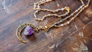 Amethyst crystal pendant necklace with a crescent moon charm resting on a wooden surface