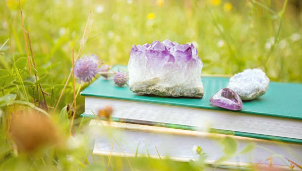 Amethyst crystal resting on stacked books in a grassy meadow with soft natural light