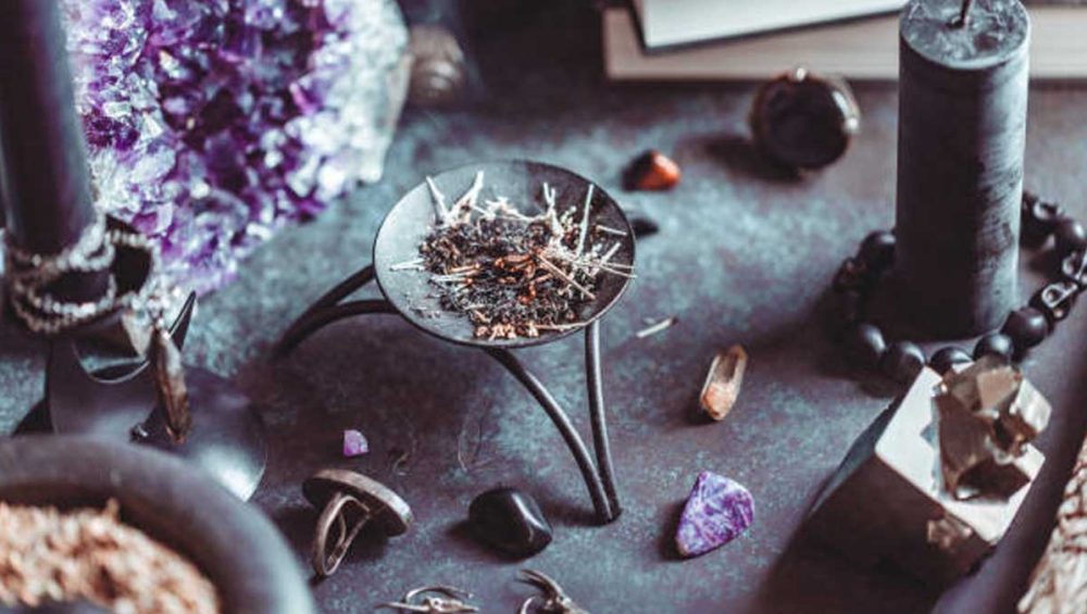 A ritual altar with an amethyst crystal, candles, herbs, and symbolic tools arranged in a dark, moody setting.