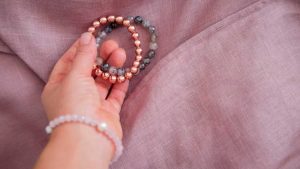 A hand holding gemstone bracelets on soft fabric