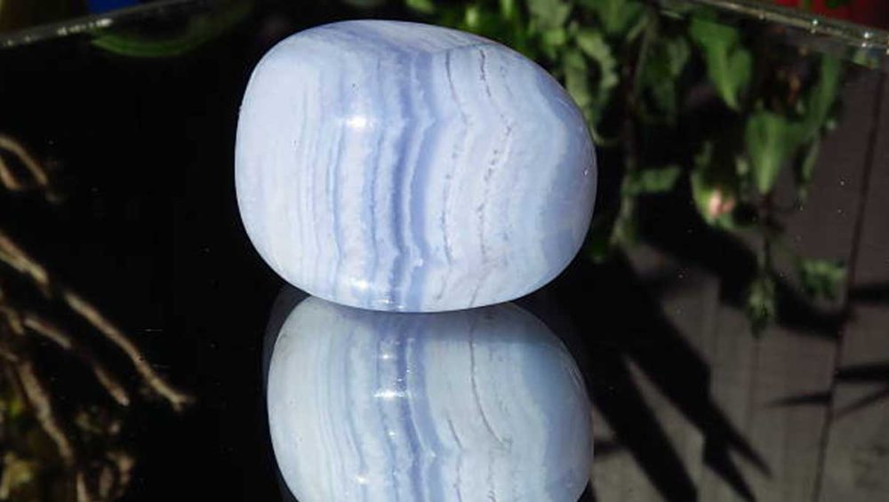 Polished blue lace agate stone with soft blue and white banding on a reflective dark surface