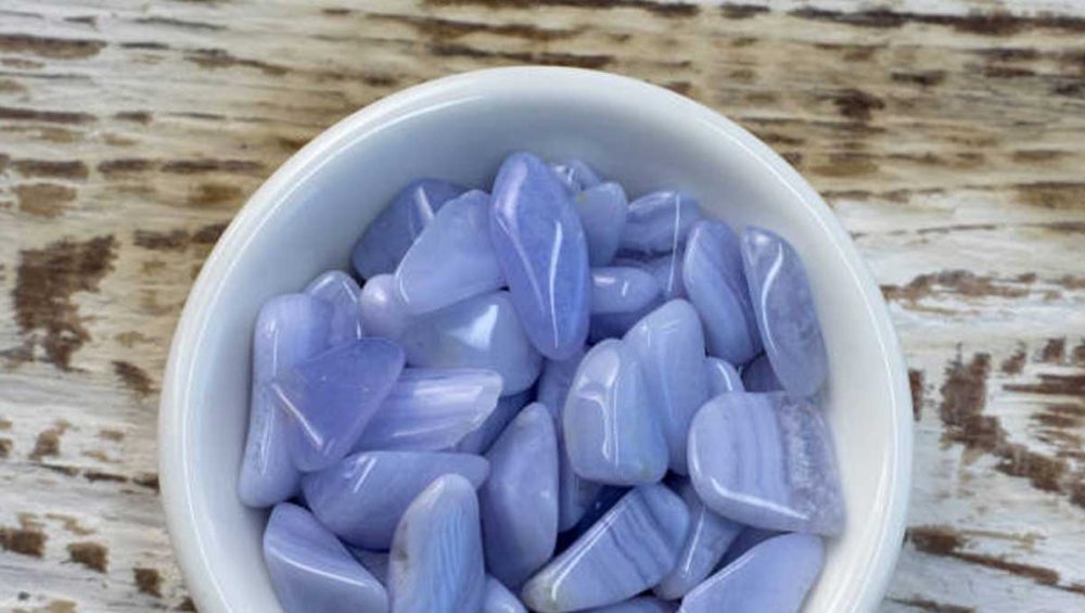 Polished blue lace agate stones resting in a white bowl on a wooden surface