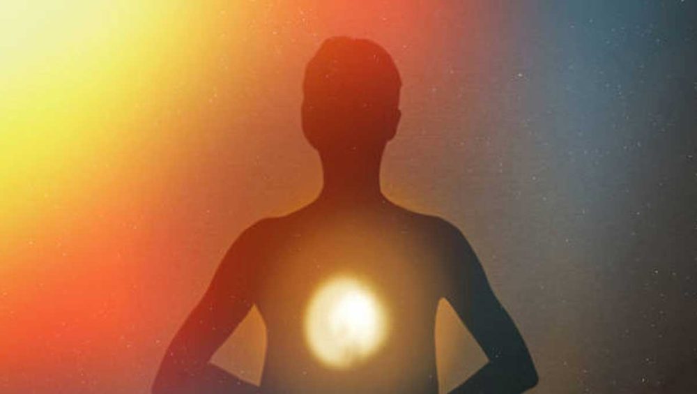Silhouette of a person with a glowing light at the center of the chest against a warm gradient background