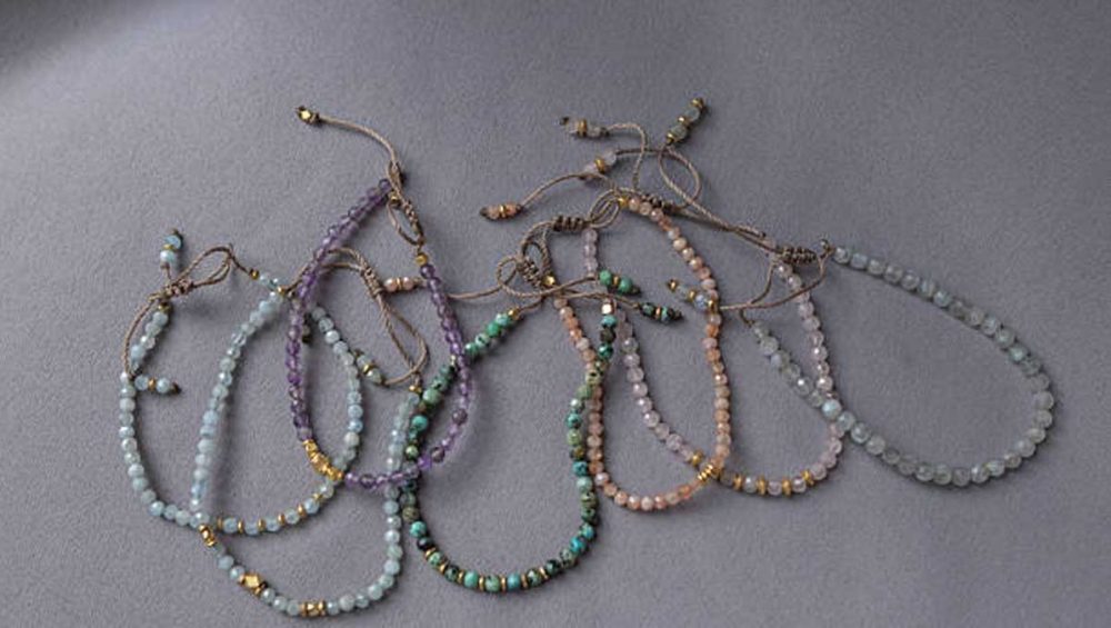 Beaded gemstone bracelets in soft pastel and earthy tones arranged on a gray background.