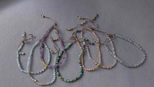Beaded gemstone bracelets in soft pastel and earthy tones arranged on a gray background.