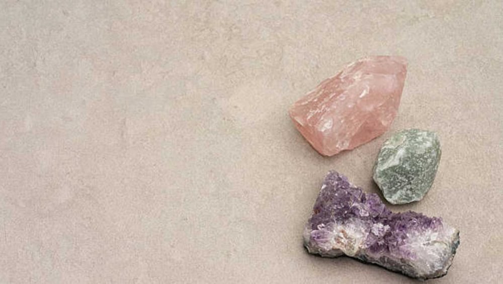 Rose quartz, green aventurine, and amethyst stones arranged on a neutral beige background.