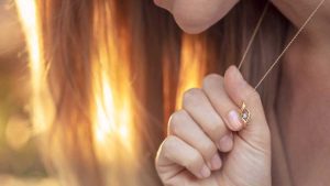 Woman holding a gold pendant necklace near her chest in warm sunset light.