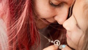 Mother and daughter touching foreheads while holding a pendant necklace together