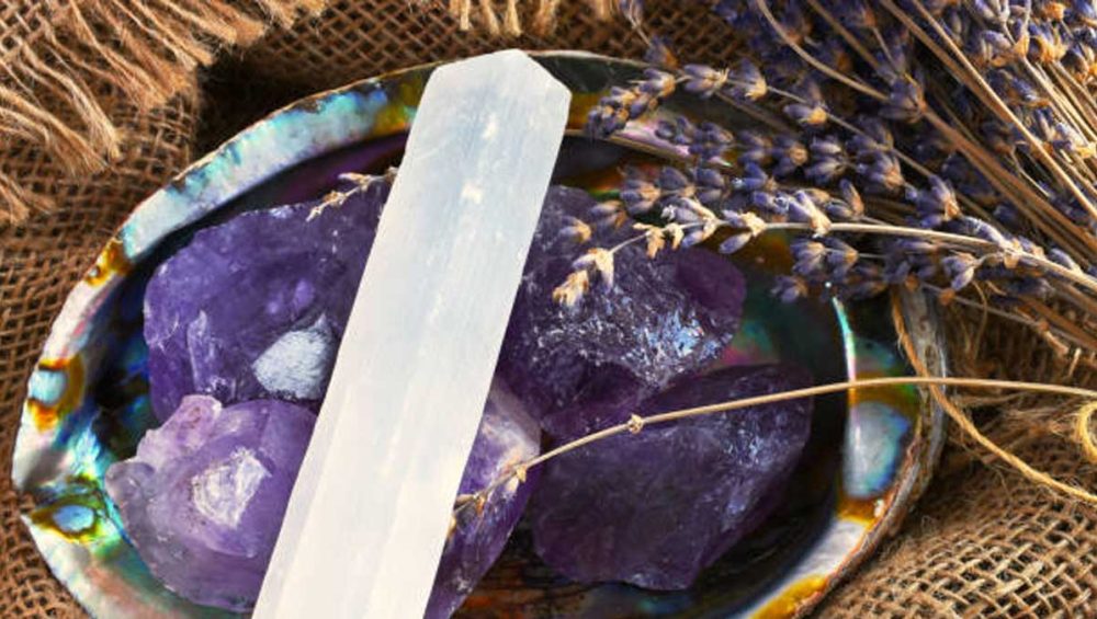Selenite wand resting on amethyst crystals inside an abalone shell with dried lavender